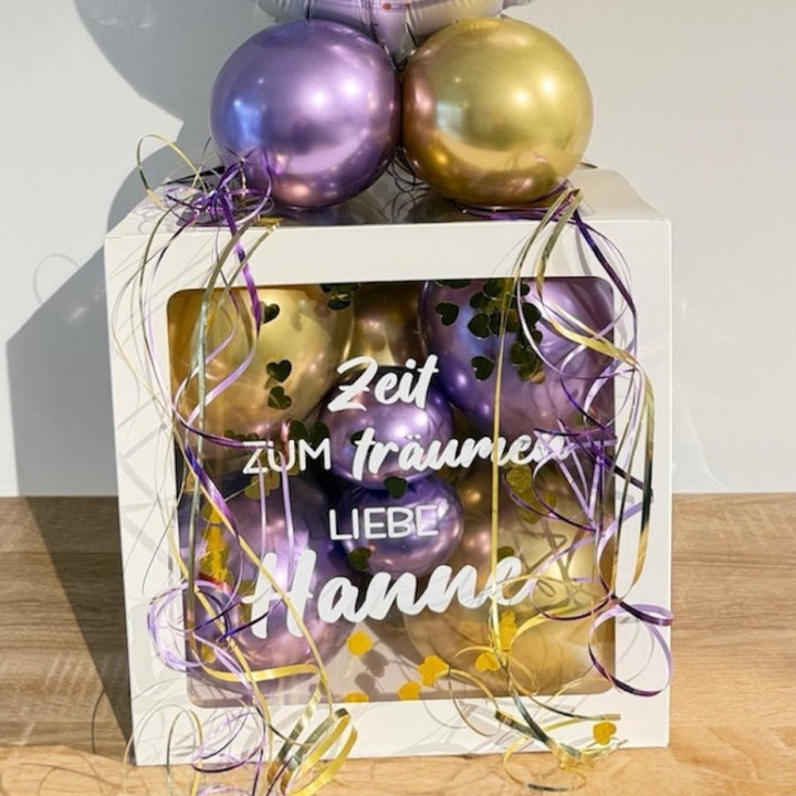 Personalisierte Ballonbox zum Ruhestand mit lila und goldenen Ballons und Folienballon „Träume gehen nie in Rente“