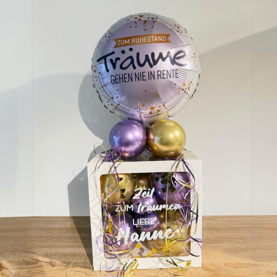 Personalisierte Ballonbox zum Ruhestand mit lila und goldenen Ballons und Folienballon „Träume gehen nie in Rente“