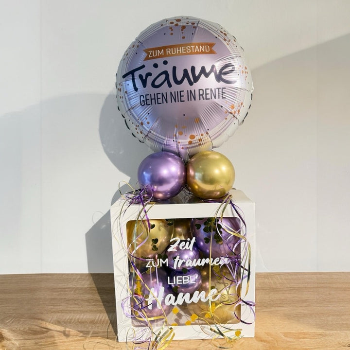 Personalisierte Ballonbox zum Ruhestand mit lila und goldenen Ballons und Folienballon „Träume gehen nie in Rente“