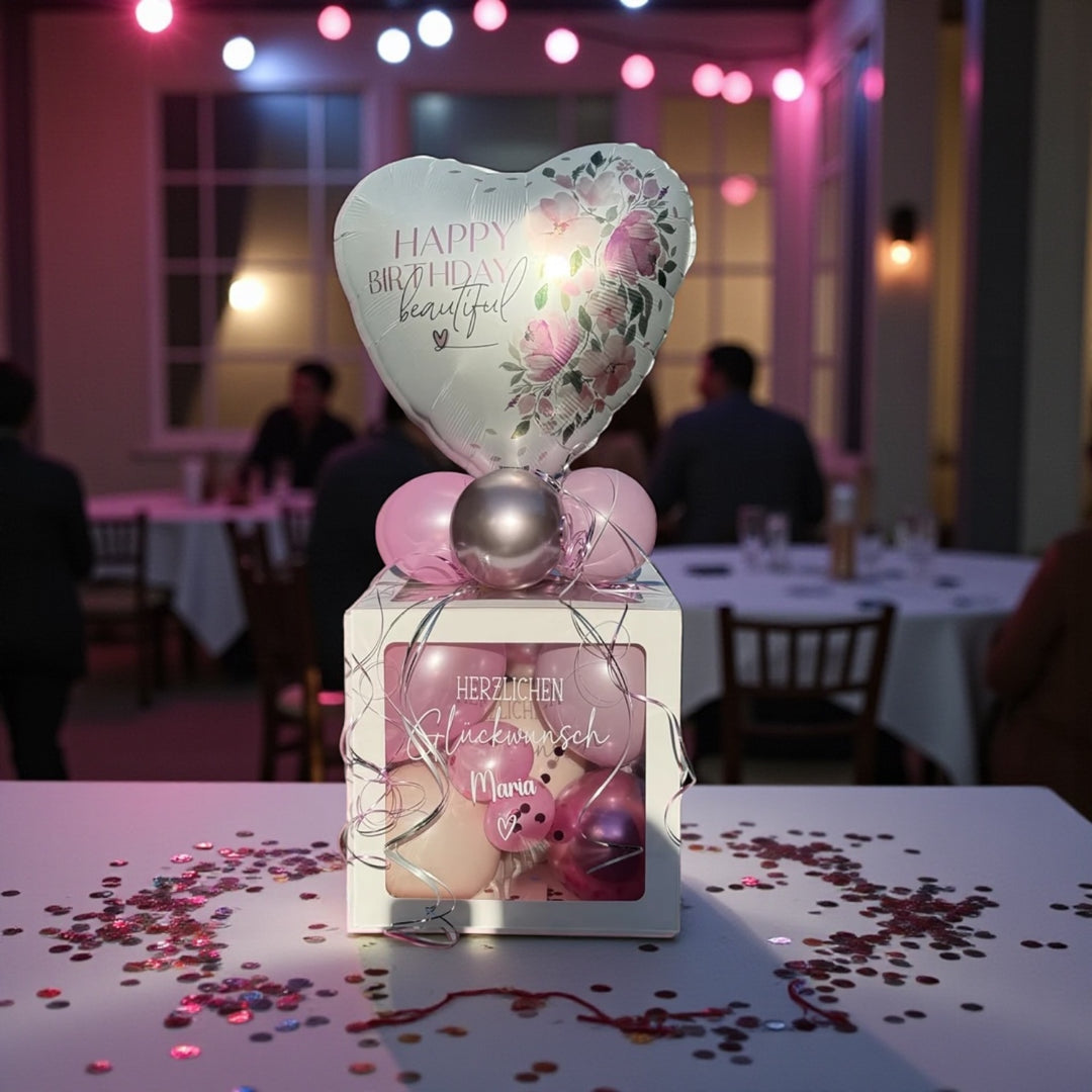 Eine weiße Ballon Box mit personalisierter Aufschrift Herzlichen Glückwunsch und einem Herzballon mit der Aufschrift Happy Birthday beautiful. Die Ballons in der Geschenkbox sind pink, rosa und silber glänzend als Geldgeschenk verpackt. 