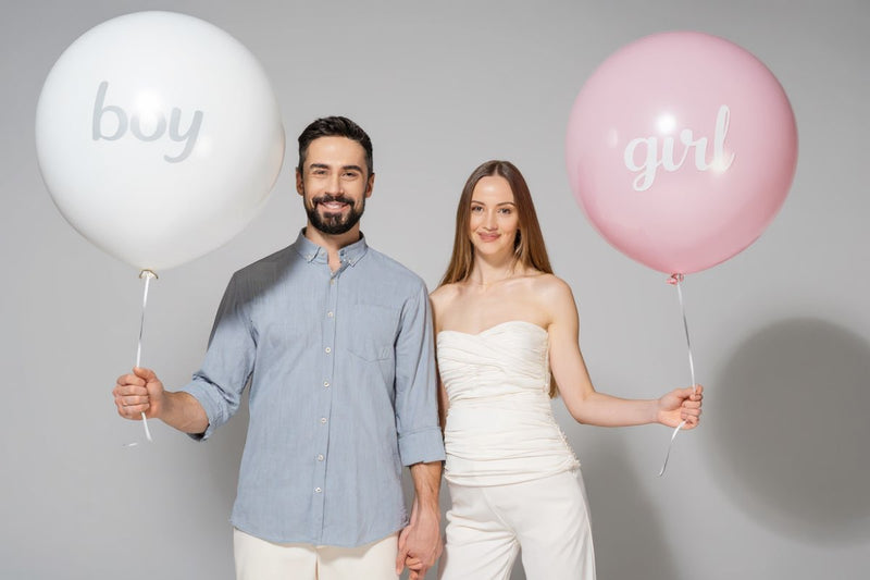 „Paar steht nebeneinander und hält große Gender-Reveal-Ballons – links weiß mit der Aufschrift ‚boy‘, rechts rosa mit der Aufschrift ‚girl‘ – perfekte Deko für Babyshower und Überraschungspartys.“