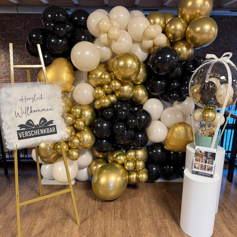 Ballon-Fotowand in Schwarz, Gold und Weiß mit Willkommensschild und Geschenkballon